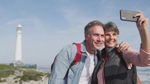 Caucasian couple enjoying free time by sea on sunny day taking photo with phone