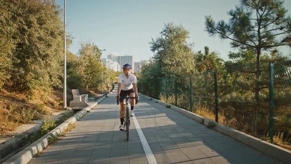 Young Girl in Protective Helmet and Sportswear is Riding Bicycle Along Tiled Bike Path in a Park