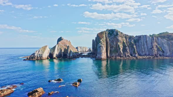 Drone flying through vertical coastal rocks jutting into sea in idyllic summer setting