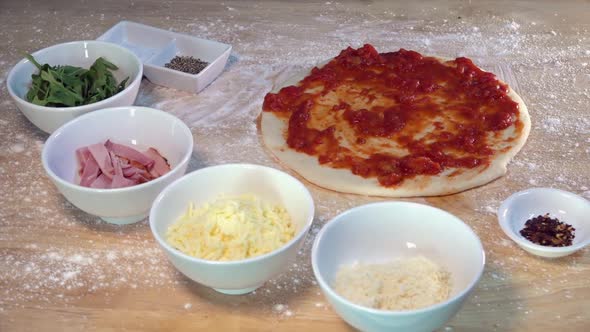 Preparing to Top a Fresh Homemade Pizza with Cheese Ham and Arugula