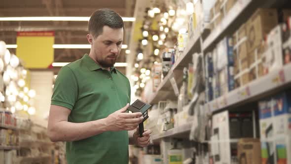 Young Male Buyer is Holding Solarpowered Lamp in Hand in Shopping Area