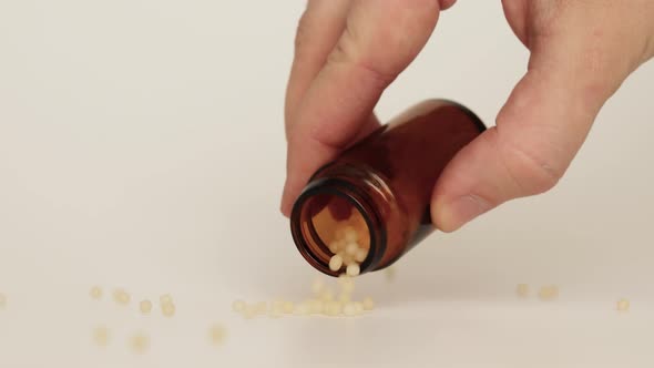 Close-up of homeopathic globules in brown glass bottle on white background