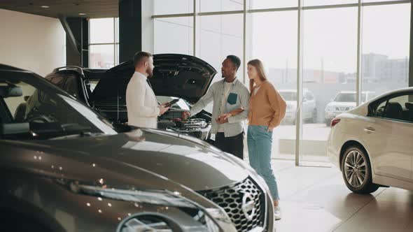 Caucasian Salesman Standing Near Luxury Car with Open Hood and Providing Details