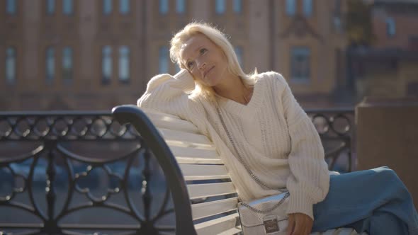 Smiling Beautiful Mature Lady Sitting on Over City Buildings Background