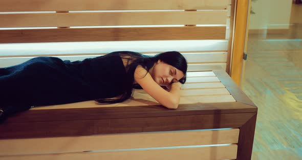 Beautiful Girl Lies on a Wooden Bench in the Sauna Behind a Glass Door