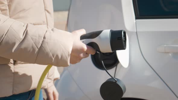 Womanplugging Power Supply Cable to Charge in the Street at Charging Point