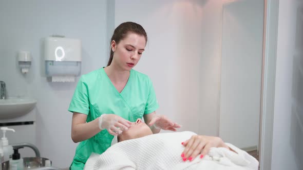 Girl Beautician Makes Facial Cleansing Procedure for Young Woman in Beauty Salon