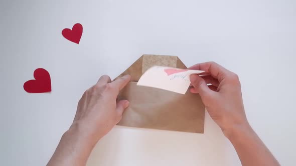 Hands Open an Envelope and Put a Red Heartshaped Valentine There for Valentine's Day