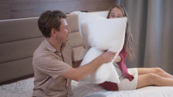 Cheerful Adult Couple Fighting Pillows and Throwing Soft Cushions at Camera in Slow Motion Laughing