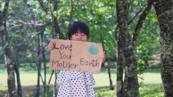 Portrait of cute little girl standing with Love Your Mother Earth poster at the summer park. alt