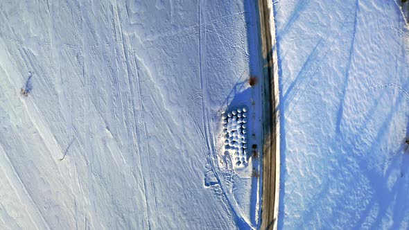 Road and hay balls on snowy field, winter aerial view