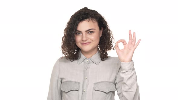 Portrait of Beautiful Woman 20s with Dark Curly Hair Expressing Gladness and Showing OK Sign Over