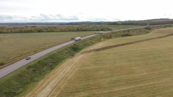 Aerial View of Trucks on Road Driving Away in Beautiful Countryside with Green Grass in Direction of