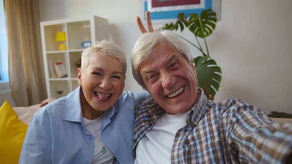 Happy Active Senior Caucasian Couple Sitting on Sofa and Taking Selfie