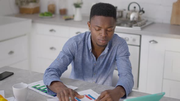 Young Tired Man Crumpling Business Graph Sitting at Kitchen Table in Home Office Sighing