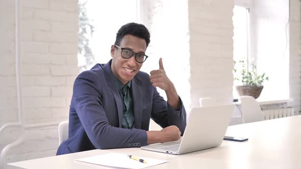 Thumbs Up By Businessman at Work Looking at Camera