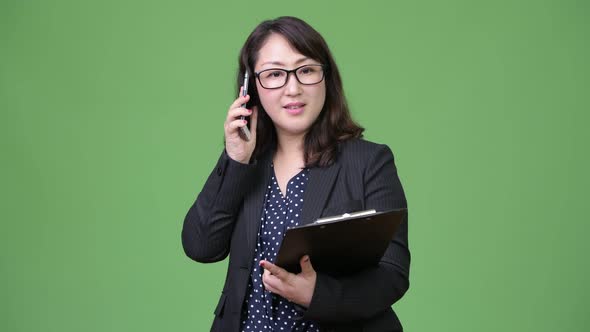 Mature Beautiful Asian Businesswoman Using Phone While Holding Clipboard