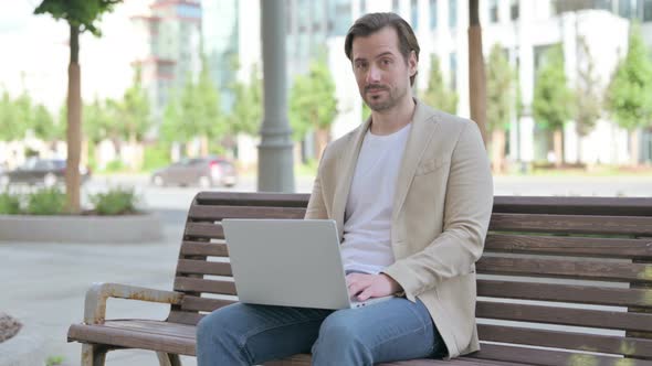 Thumbs Down By Young Man with Laptop Sitting on Bench