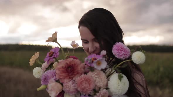Portrait of a Charming Happy Bride with a Large Bouquet of Dahlias Near Her Face on a Blurred