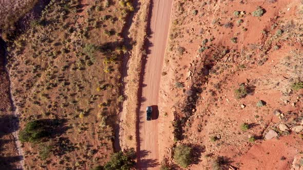 Dark SUV Drives On Dirt Dusty Road Crossing A Red Sand Desert On A Sunny Day