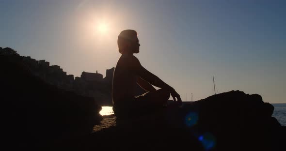 Silhouette of a boy does yoga on the rocks at sunset