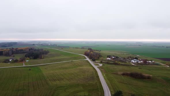 Aerial top shot of a small but long country road with green meadow surrounding it.