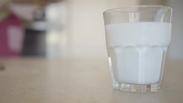 Close-up Glass of Milk on the Table on the Background a Young Woman Pulling Out Freshly Baked Buns