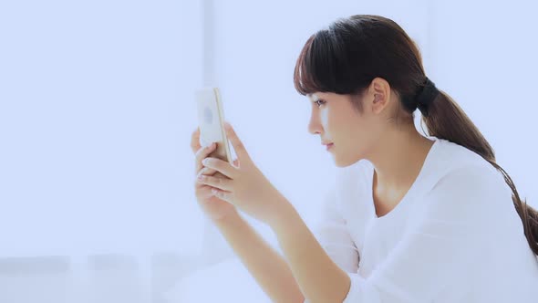 Beautiful young asian woman sitting taking a selfie with smart phone on bedroom.
