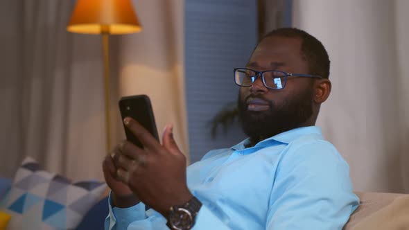 African Businessman Using Smartphone While Sitting on Sofa at Home