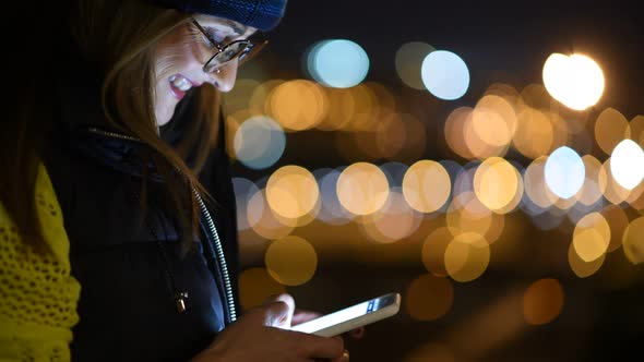 Woman using mobile phone at night with city lights as background