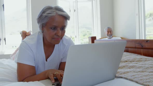 Front view of senior black woman lying on bed and using laptop in bedroom of comfortable home 4k