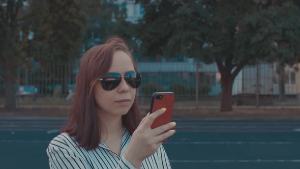 Young Woman in Sunglasses with Mobile Phone on Street in Summertime