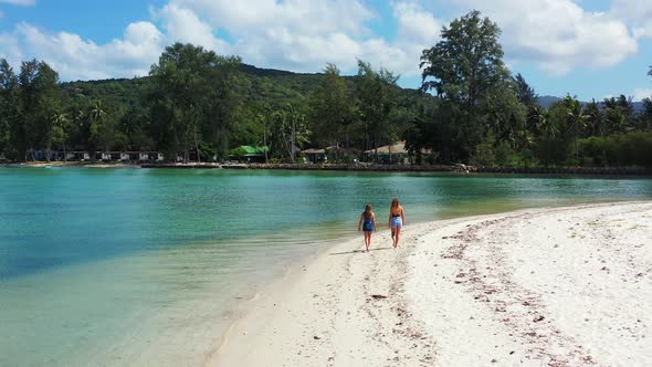 Mother and daughter walking along the sandy beach. Calm Thailand lagoon with aquamarine water and un