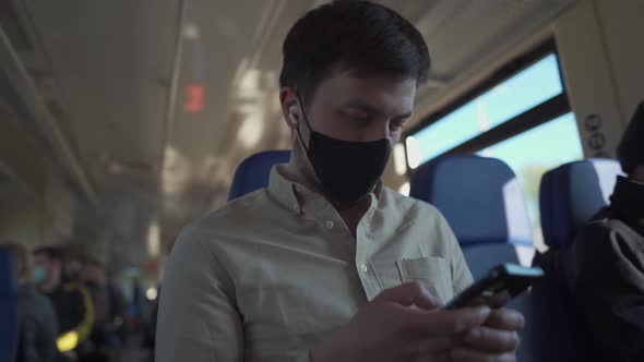 Caucasian Man in Black Mask Listens to Music on Headphones and Uses Smartphone While Traveling on