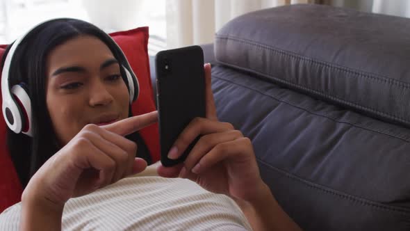 Mixed race gender fluid person sitting on couch using smartphone and listening to music at home