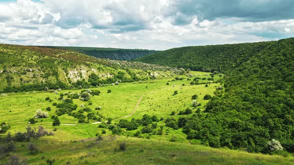 Aerial drone view of a valley in Moldova. River, a lot of greenery, cloudy sky