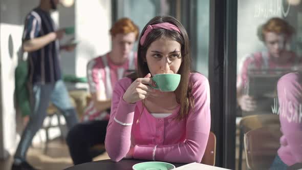 Front View of Confident Charming Young Retro Woman Drinking Coffee Looking Out the Window in Vintage