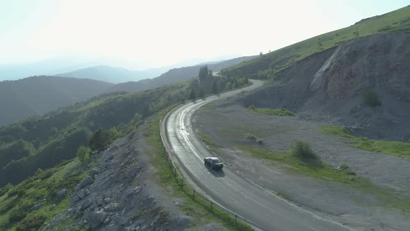 One Black Car Driving on Sunny Mountain Road