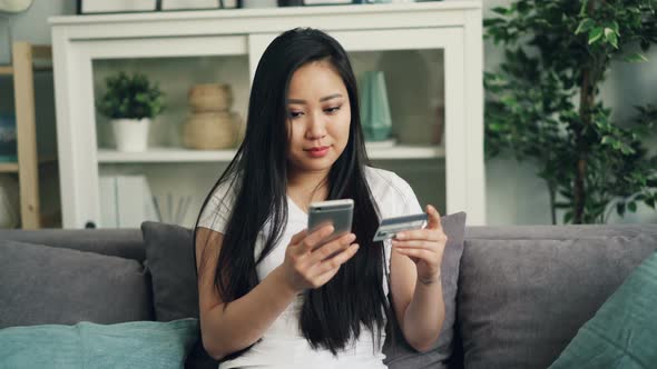 Young Lady Is Making Online Payment Holding Bank Card and Touching Smartphone Screen