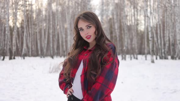Young Woman with Wavy Hair Standing and Touching Face in Winter Forest