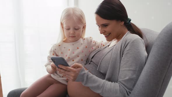 Caucasian woman in advanced pregnancy and her elementary aged daughter using mobile phone at home. S