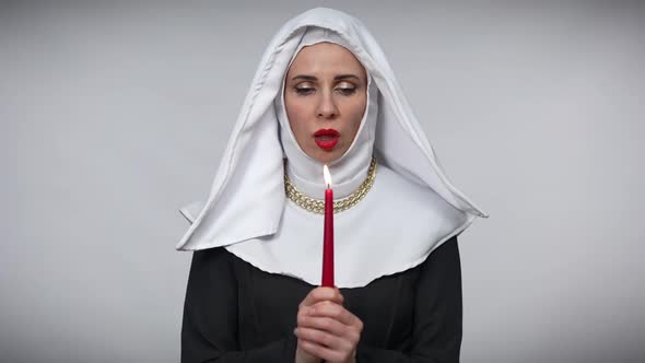 Portrait of Woman in Nun Costume Blowing Out Candle Looking at Camera with Dissatisfied Aggressive