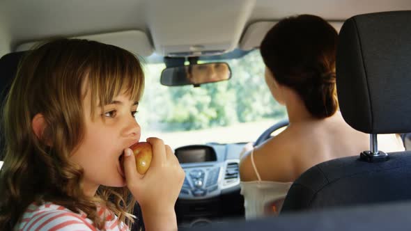 Girl having apple in the back seat of the car