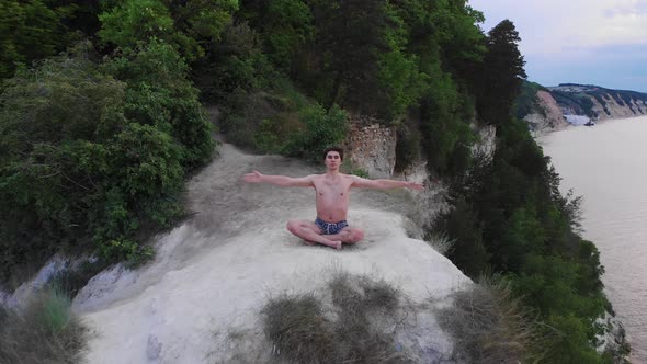 Young Shirtless Man Meditating on a Cliff at Early Morning