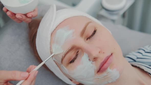 Closeup Shot of Cosmetician Hands Applying Cream Mask on Young Woman's Face at Beauty Spa Salon