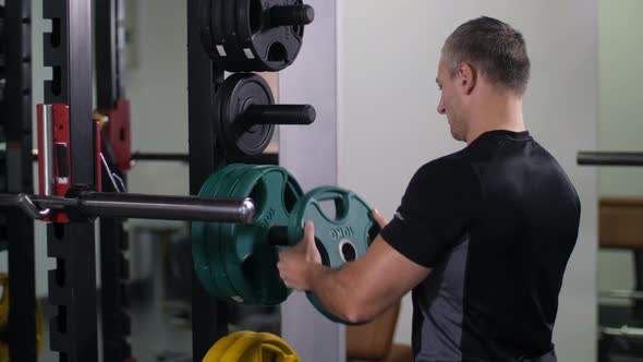 Handsome Strong Man Puts a Disk on the Barbell Turns to the Camera and Smiles  Slow Mo