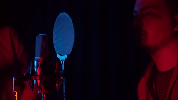 Two Men Sits Down in Neon Lighting and Starts Recording a Song