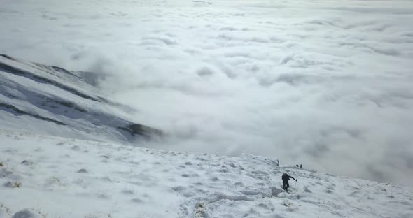 Aerial drone view of men hiking in the clouds and snow covered mountains in the winter.