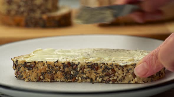 Yummy Appetizing Snack. Female Hands Using Knife To Spread Butter Onto a Slice of Bread with Seeds. 