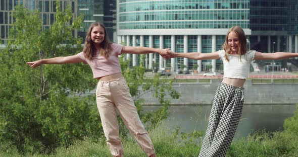 Happy Young Girls Holding Hands on Embankment in City